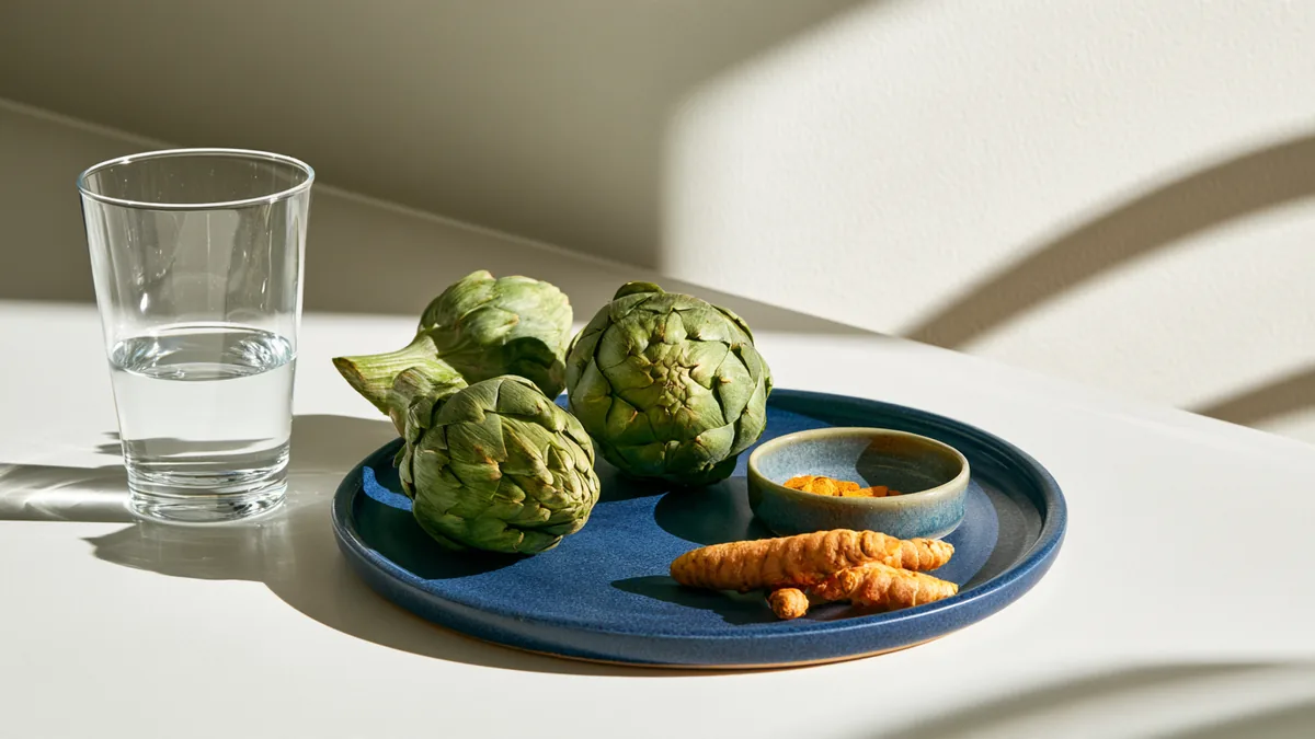 Verre d'eau, artichauts frais et curcuma sur un plan de travail clair, pour soutenir le foie au quotidien